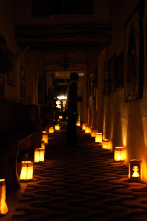 A dimly lit hallway with glowing lanterns lining the floor and a silhouette of a person in the background.