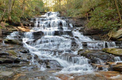 A serene waterfall cascading over rocky steps, surrounded by lush greenery and dappled sunlight.
