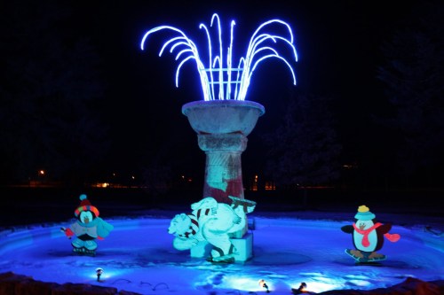 A brightly lit fountain at night, featuring animated characters like a penguin and a snowman around the base.