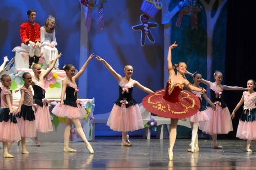 A ballet performance featuring dancers in pink tutus, with one dancer in a red dress, on a colorful stage.