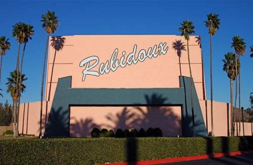 Sign for Rubidoux with palm trees in front, set against a pink building. Clear blue sky above.