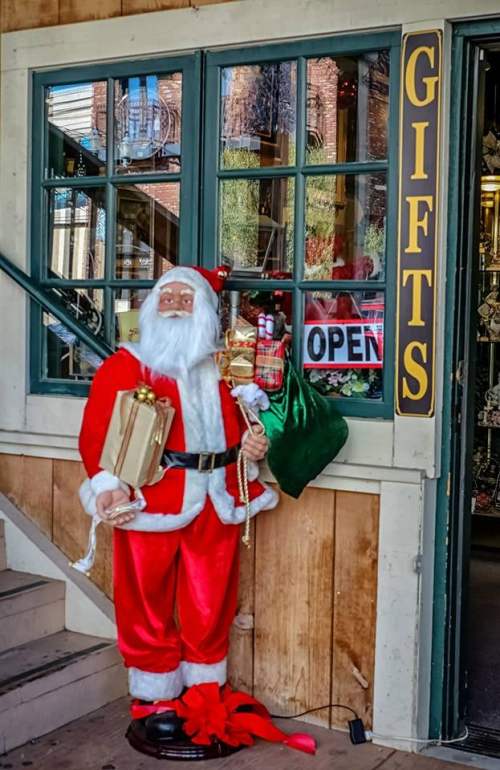 A festive Santa Claus figure stands by a gift shop entrance, holding presents and a bag, with an "OPEN" sign in the window.
