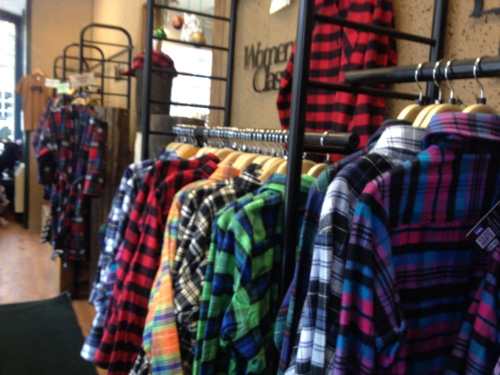 A display of colorful plaid shirts hanging on racks in a women's clothing store.