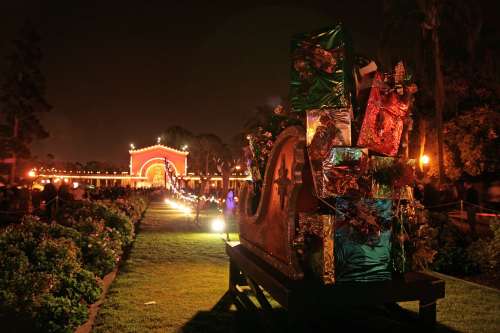 A festive night scene with colorful decorations and lights along a pathway leading to an archway.