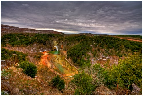 A panoramic view of a lush, green valley with a waterfall and cloudy skies above.
