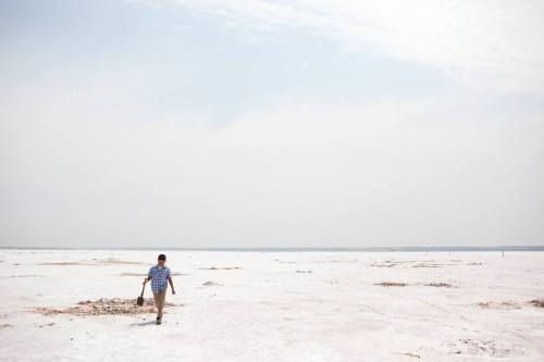 A person walks alone across a vast, dry, white landscape under a cloudy sky.