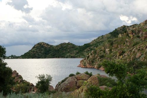 A serene landscape featuring rocky hills beside a calm lake under a cloudy sky.