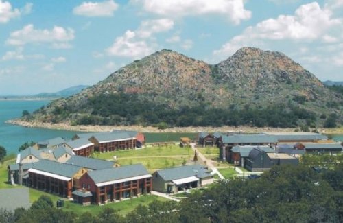 Aerial view of a lakeside facility surrounded by hills and greenery, featuring multiple buildings and open spaces.