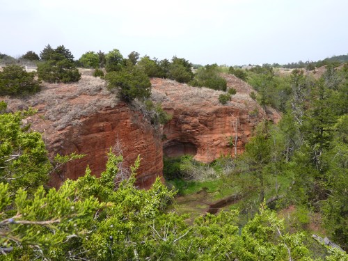 A scenic view of red rock formations surrounded by greenery and trees, with a small valley below.