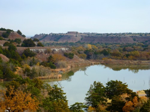 A serene landscape featuring a calm lake surrounded by autumn-colored trees and rolling hills in the background.