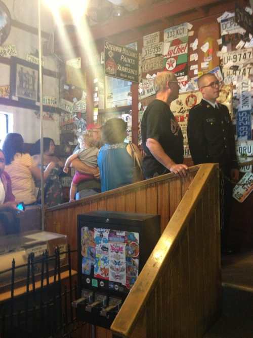A busy restaurant interior with people, including a child, and walls adorned with various stickers and signs.