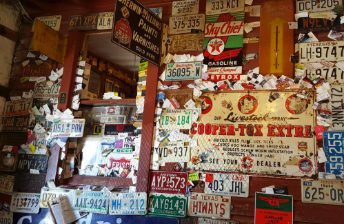 A cluttered wall filled with vintage signs, license plates, and advertisements in a rustic setting.