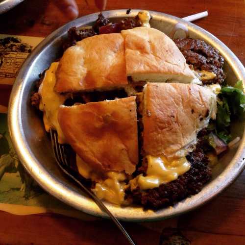 A metal plate with a sandwich made of two toasted buns filled with meat and melted cheese, served with lettuce.