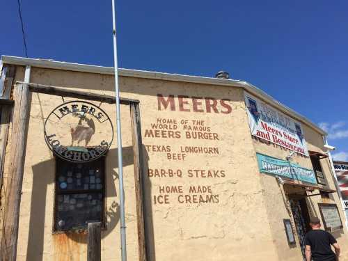 Exterior of Meers restaurant featuring signs for burgers, steaks, and homemade ice creams against a rustic wall.