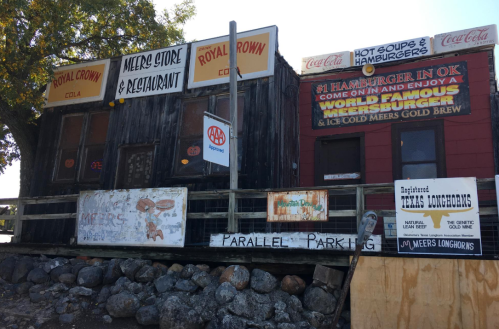 A rustic building with various signs for a store and restaurant, featuring advertisements for burgers and drinks.