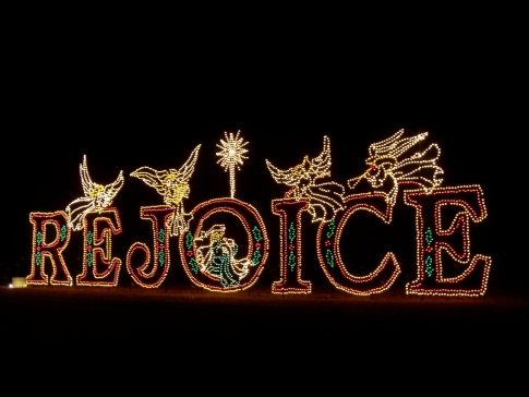 Colorful holiday lights spell out "REJOICE" with decorative elements, set against a dark background.