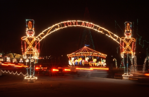 Colorful holiday lights form an arch with toy soldiers, leading to a festive carousel in a nighttime scene.