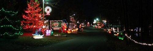 A festive street lined with colorful Christmas lights and decorations, including trees and holiday figures, at night.