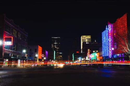 Colorful city lights illuminate buildings at night, with streaks of light from passing cars.