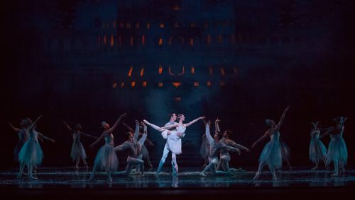 A ballet performance featuring dancers in elegant costumes, with a central couple in a dramatic pose on stage.