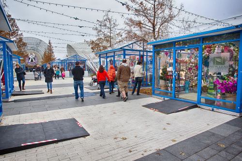 A bustling outdoor market with blue stalls, people walking, and festive decorations in a cloudy atmosphere.