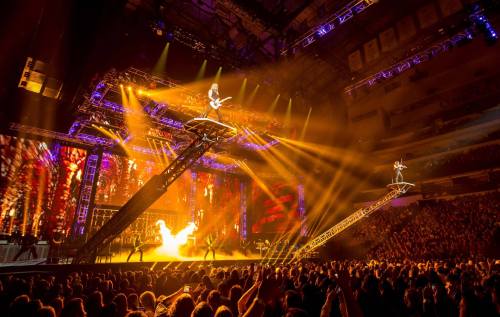 A vibrant concert scene with a guitarist on a raised platform, dramatic lighting, and a cheering crowd below.