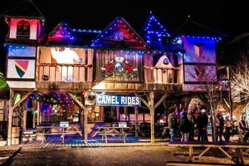 A festive building at night, adorned with colorful lights and a sign for camel rides, with people gathered outside.