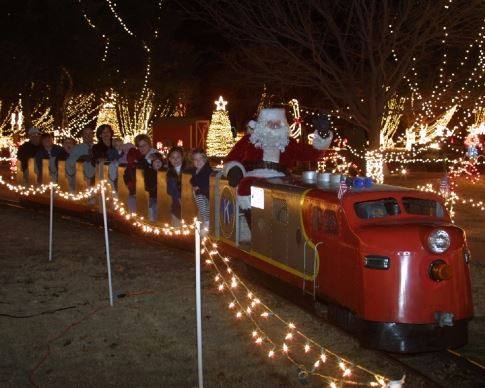 A festive train with Santa and children, surrounded by colorful holiday lights and decorations.