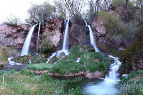 A serene landscape featuring multiple waterfalls cascading over rocky cliffs, surrounded by lush greenery and flowing water.