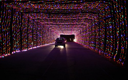 A car drives through a brightly lit tunnel adorned with colorful holiday lights.