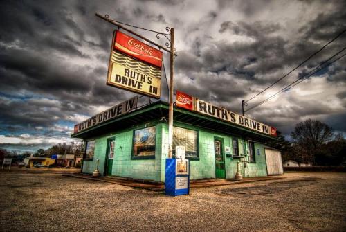 A vintage drive-in diner with a green exterior and a Coca-Cola sign, set against a dramatic cloudy sky.