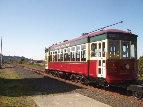 A vintage red and cream trolley car on a railway track under a clear blue sky.