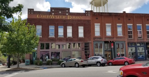Exterior of ColdWater Books, a brick building with large windows, surrounded by parked cars and trees.