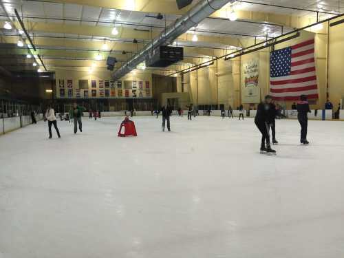 A busy ice skating rink with skaters of all ages gliding on the ice, featuring an American flag in the background.