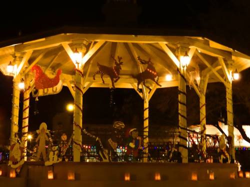 A festive gazebo decorated with lights and holiday figures, illuminated at night.