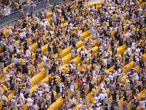 A large crowd of fans in black and gold attire cheering enthusiastically in a stadium.