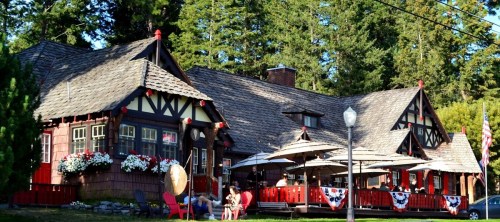 A charming lodge with a wooden exterior, surrounded by trees and featuring outdoor seating and decorative flowers.