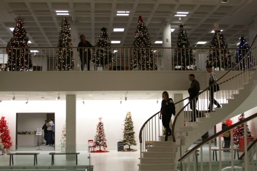 People walk down a spiral staircase in a festive space decorated with Christmas trees and lights.