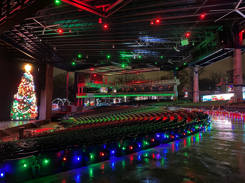 A festive venue with colorful lights, a decorated Christmas tree, and empty rows of seats under a covered stage.