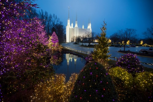 A beautifully lit temple surrounded by colorful Christmas lights and trees, reflecting in a calm pond at dusk.
