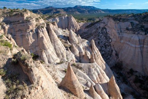 A scenic view of unique rock formations and spires in a canyon landscape under a blue sky with scattered clouds.