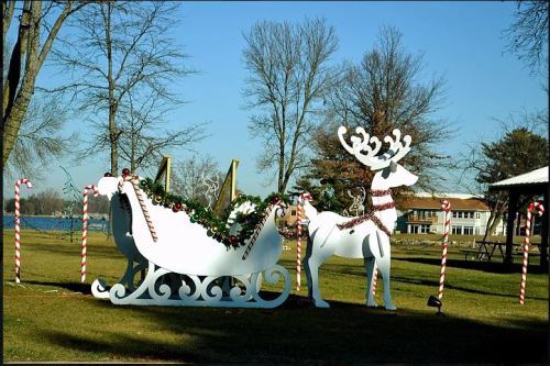 A festive display featuring a white sleigh and reindeer, surrounded by candy canes and trees by a lake.