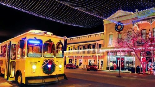 A festive yellow trolley parked on a street adorned with colorful holiday lights and decorations at night.