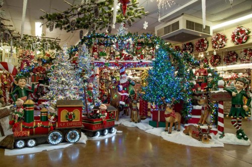 A festive holiday display featuring a train, elves, a decorated tree, and colorful lights in a cheerful setting.