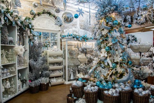 A festive display featuring a decorated Christmas tree, silver and blue ornaments, and holiday decorations in a cozy shop.