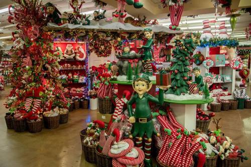 A festive holiday display featuring elves, Christmas trees, and colorful decorations in a cheerful store setting.