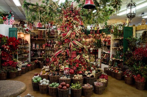A beautifully decorated Christmas tree surrounded by festive decorations and baskets of ornaments in a cozy shop.
