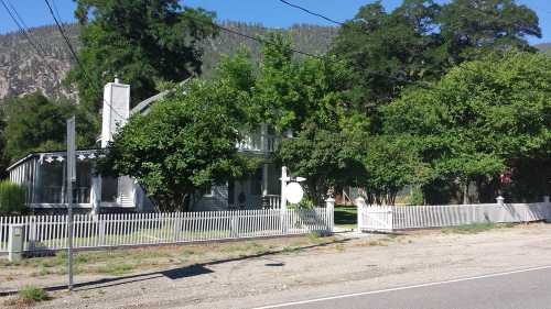 A large house surrounded by trees and a white picket fence, set against a mountainous backdrop.