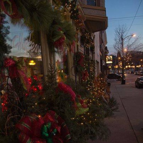 A festive storefront decorated with greenery and lights, set against a twilight sky and a quiet street.