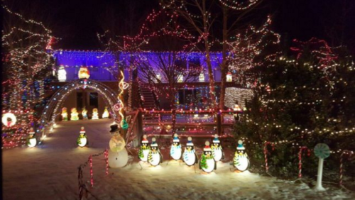 A festive scene with colorful Christmas lights, snow, and illuminated snowmen lining a pathway to a decorated house.